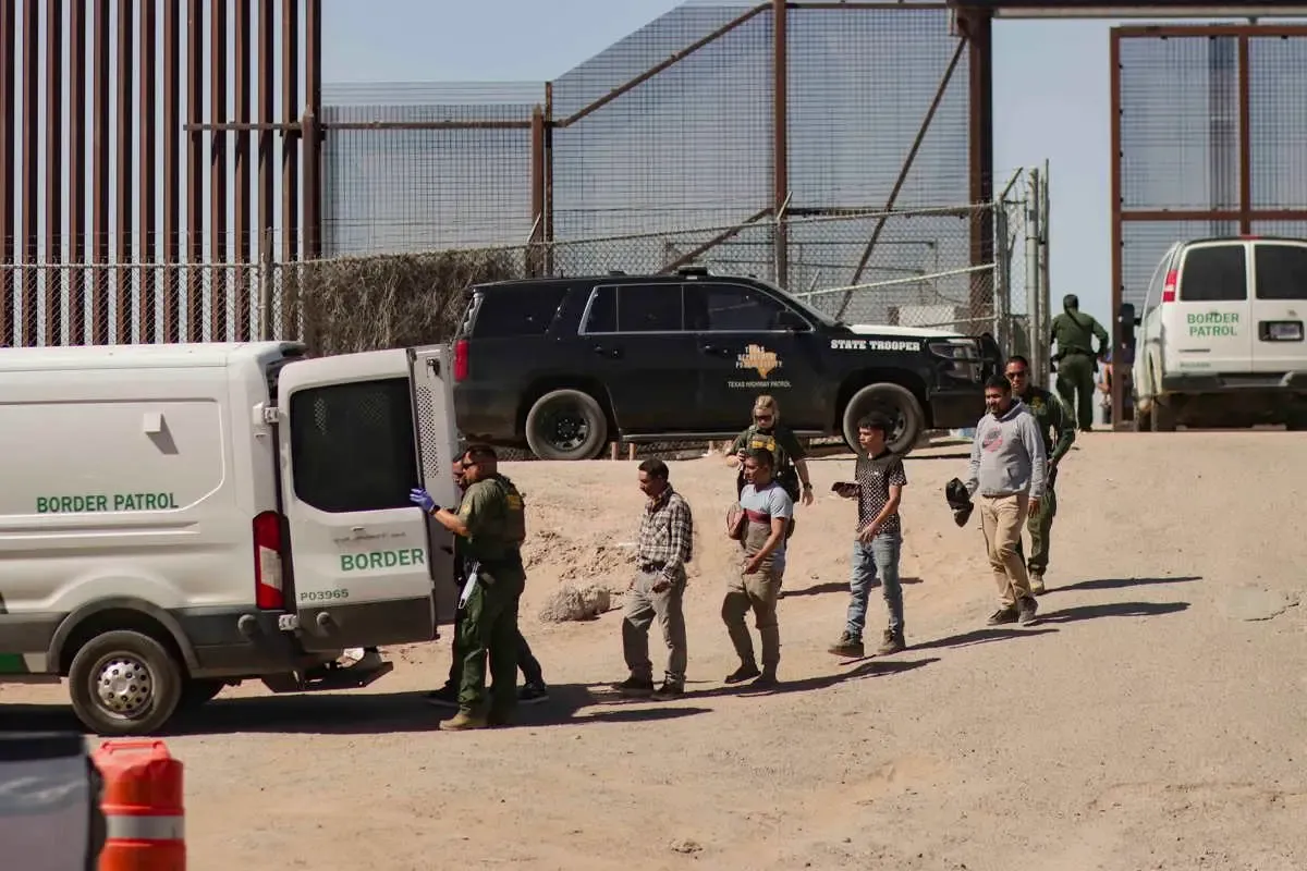 EL PASO. Migrantes detenidos son llevados por miembros de la Patrulla Fronteriza estadounidense a un vehículo, junto al muro