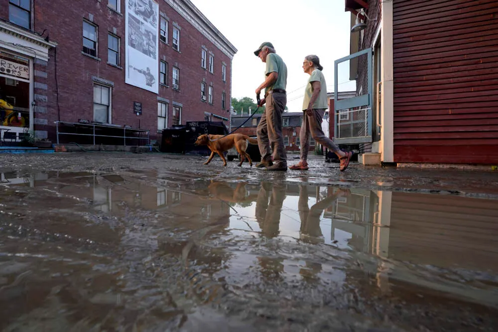 La gente pasea a un perro en una calle embarrada el martes 11 de julio de 2023 en Montpelier, Vt. Una tormenta que arrojó has